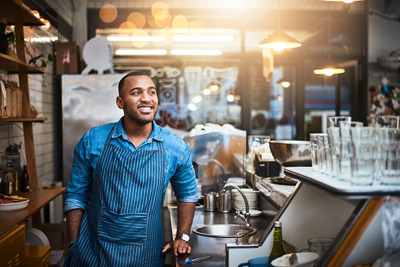 Addressing regional inequality through SME lending Barista stands smiling behind coffee bar, light shining from above