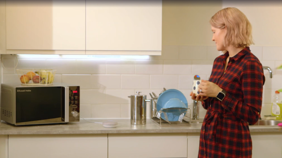 woman holding a mug in a kitchen and speaking to a Google Assistant device